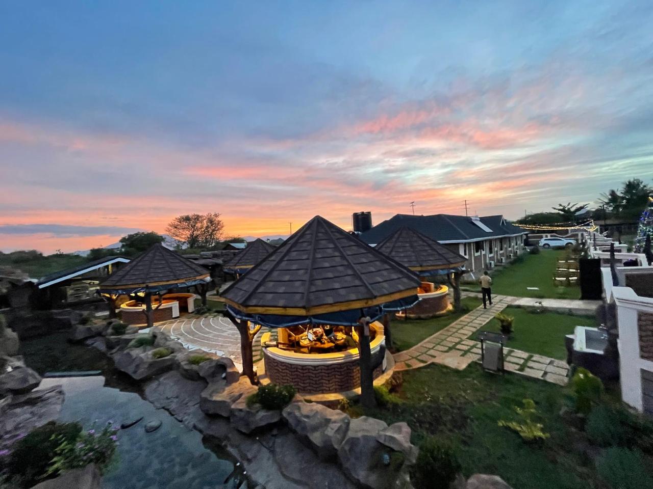 Mawimbi Jiko grounds at dusk with lantern-lit gazebos, paved terrace and the rock water feature